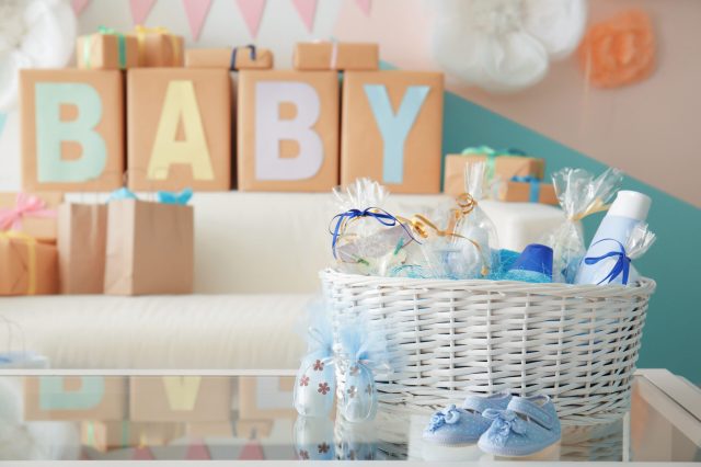 Wicker basket with gifts for baby shower party on table indoors